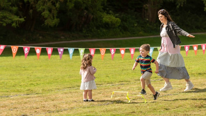 An adult running on the lawn with two small children playing on the grass
